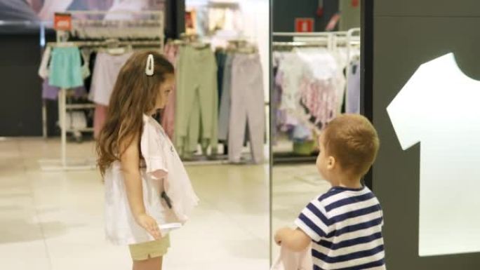 商店里的两个小孩在购物中心的服装店里为自己挑选东西。商店里的人选择时尚的衣服。孩子们在没有父母监督的