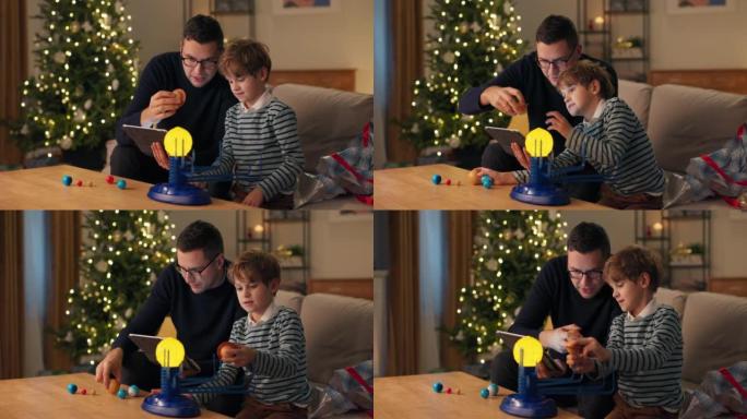 雄心勃勃的人在圣诞节期间与学龄儿子共度时光，爸爸教孩子有关行星系统的知识，他们将玩具模型组装在一起，