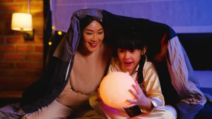 亚洲母女俩在床上一起享受不同颜色的轻球的乐趣，他们在假期之夜呆在家里看起来很开心