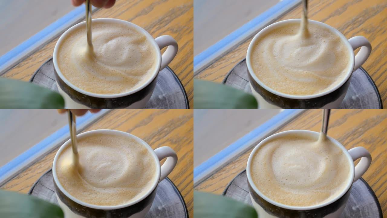 一杯卡布奇诺咖啡的特写镜头，上面放着美味的牛奶泡沫，女人的手用勺子搅动。咖啡大满贯期间在餐厅喝咖啡。