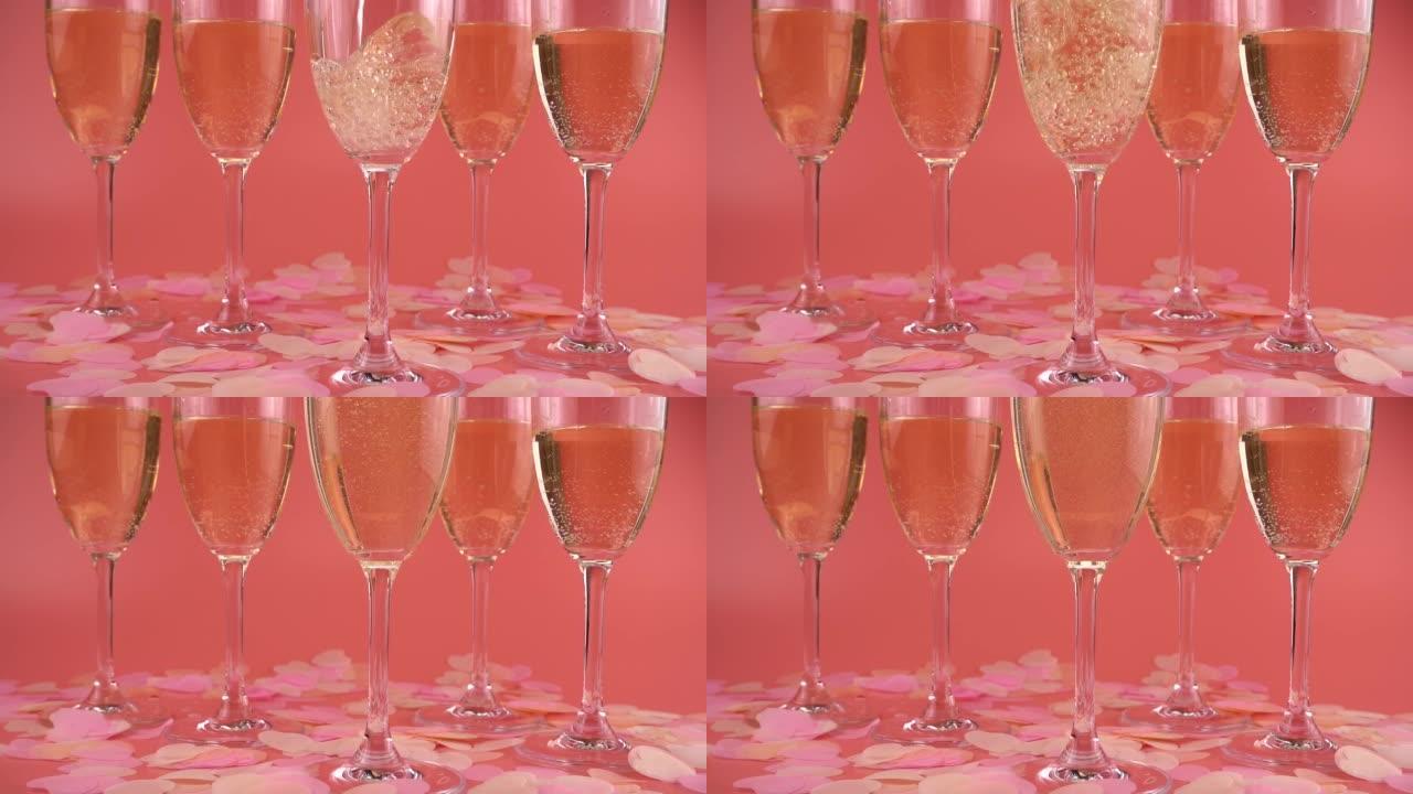 将起泡酒倒入带有心形五彩纸屑的粉红色背景的玻璃杯中。慢动作。