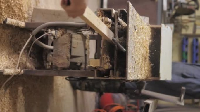 垂直视频。车间的木匠在木工机器上工作，加工和对齐木材以制造家具零件。木板加工后出来，锯末。4k