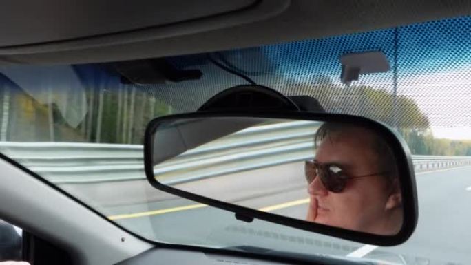 戴墨镜的人在空旷的道路上开车关闭镜子视图