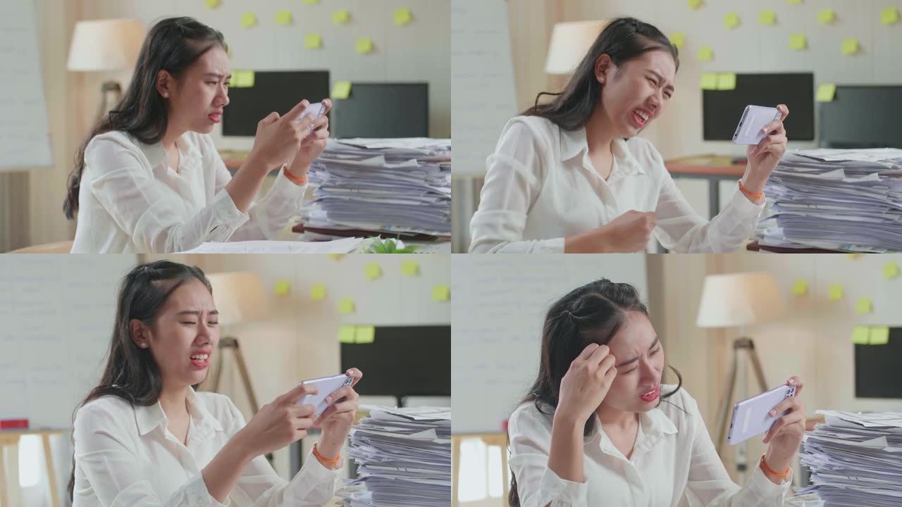 亚洲女性在办公室处理文件后在智能手机上输掉比赛的特写镜头