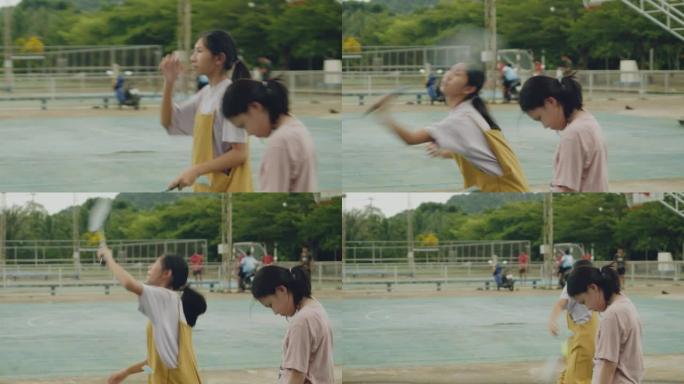 哭泣的亚洲女孩站着不动，而姐姐在室外球场上打羽毛球。生活方式概念。