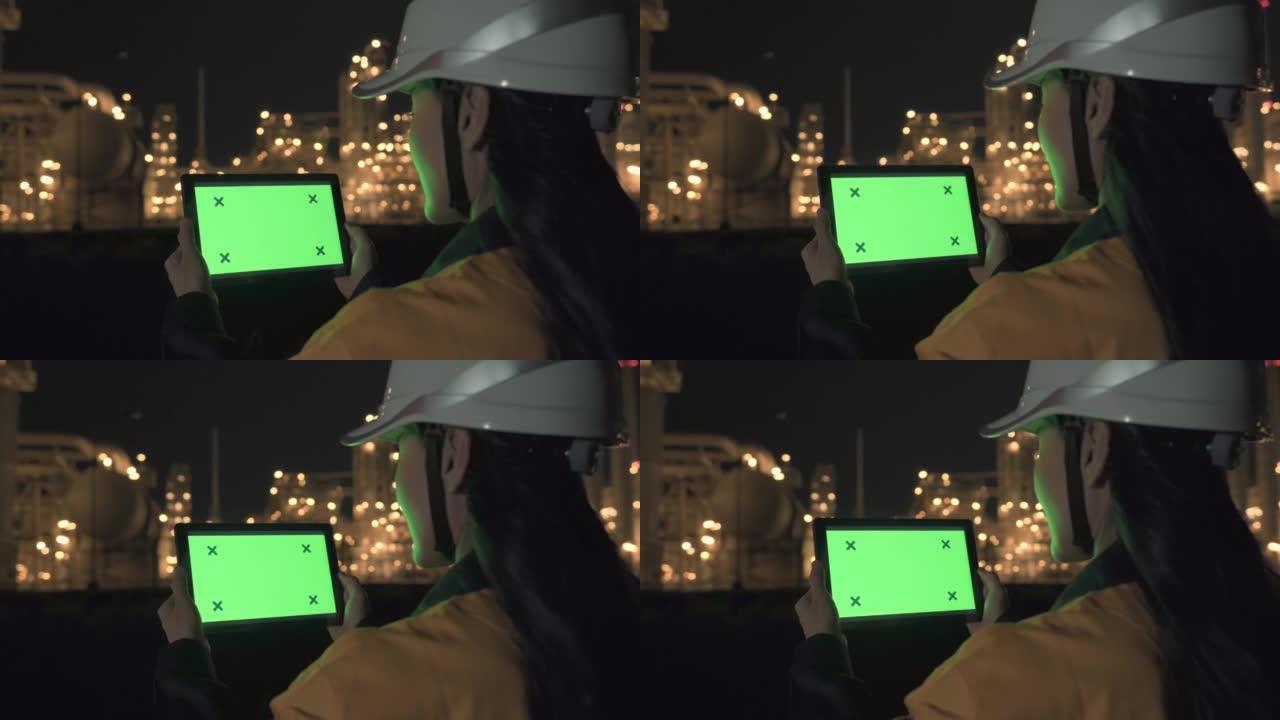亚洲女性检测工程师晚上在石油和天然气精炼厂工业工厂内拿着绿色屏幕的数字平板电脑
