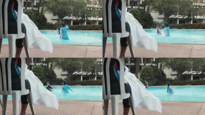两个亚洲兄弟姐妹女孩在游泳池里一起玩水，父母在旁边看着。孩子们在游泳池里一起嬉戏玩耍。