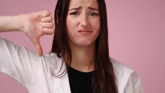 4k视频，年轻女子在粉红色背景上显示拇指向下手势。