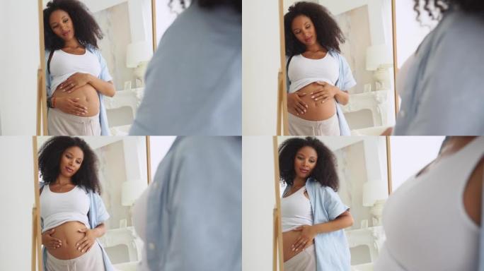 黑人孕妇早上在镜子里欣赏她的肚子。享受积极的情绪。黑人年轻美丽的未来母亲在家里快乐地抚摸着她的肚子。