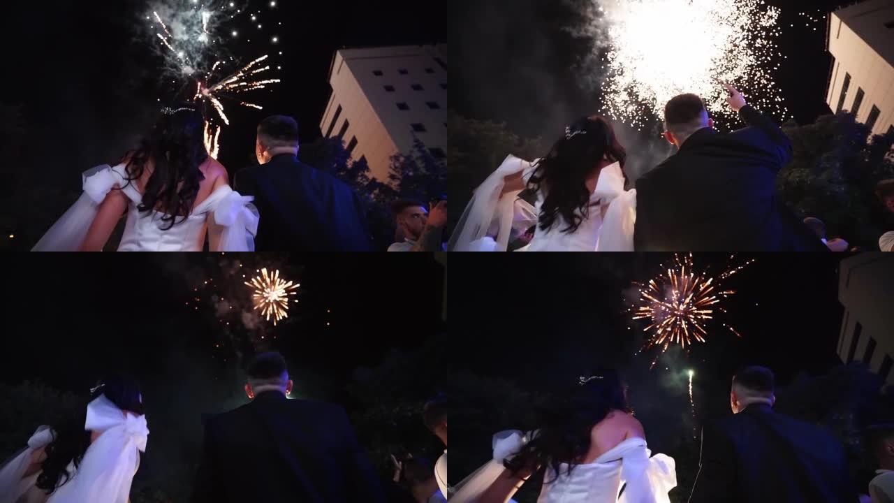 新郎和新娘在天空观看烟花。恋爱中的情侣在婚礼结束时接吻。兴奋的客人看着火展。