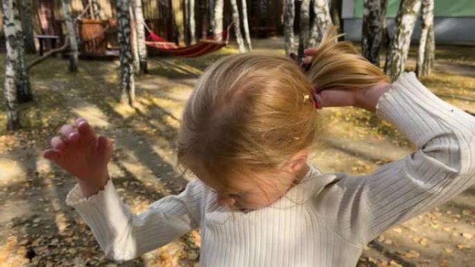 小女孩在金色的秋天从金色的头发上取下干燥的落叶