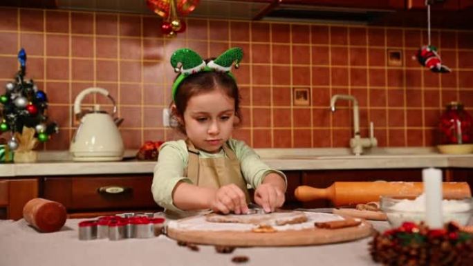 可爱的小女孩头上有精灵箍，围裙站在厨房岛，用姜饼面团切模