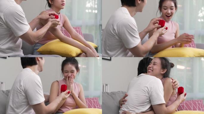 快乐的亚洲男人在家里的客厅给女人用红色小盒子送订婚戒指。