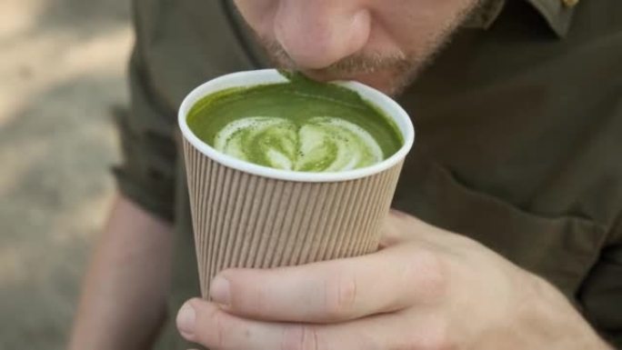 男子在夏季咖啡馆户外用一次性纸杯喝抹茶拿铁绿茶。健康饮料