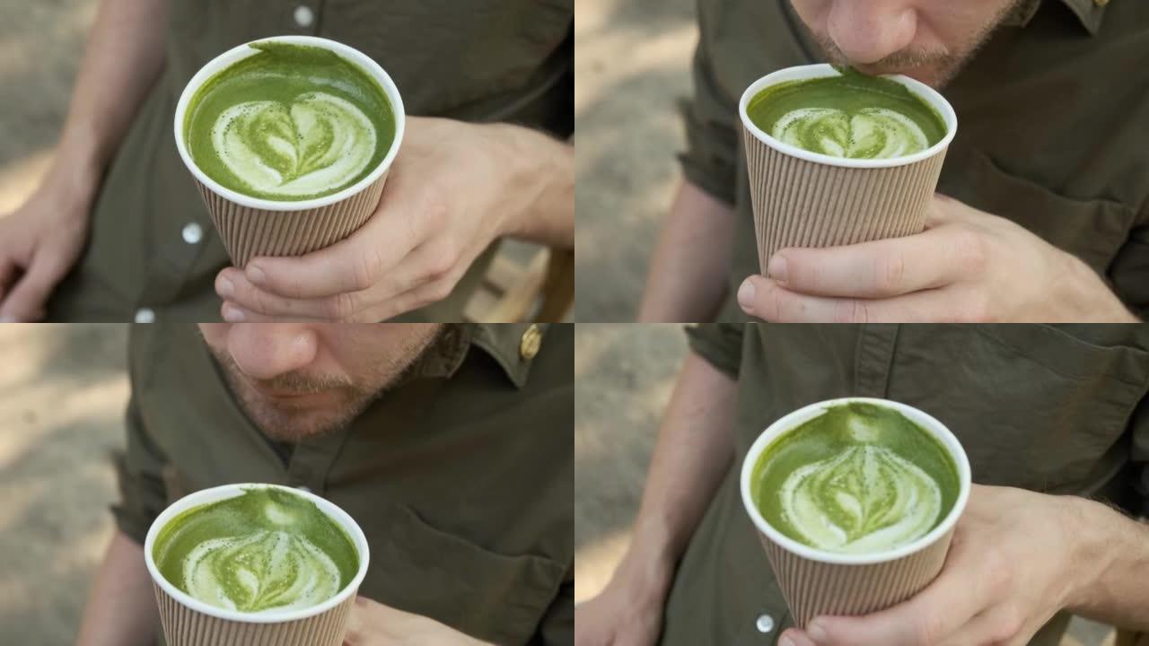 男子在夏季咖啡馆户外用一次性纸杯喝抹茶拿铁绿茶。健康饮料