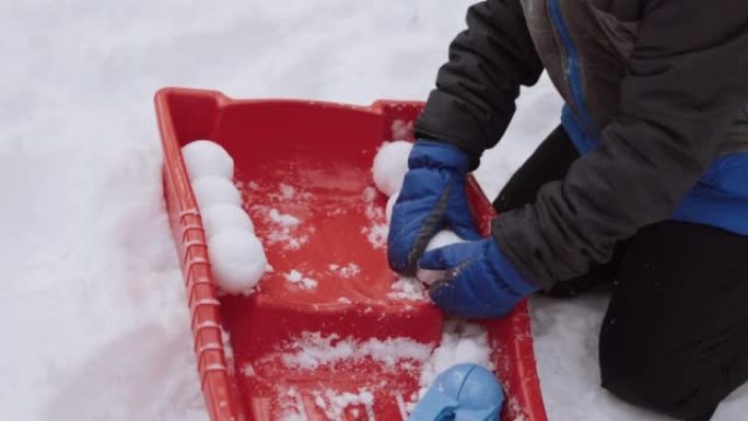 穿着连指手套的孩子用红色雪橇摆出圆形雪球，特写镜头。