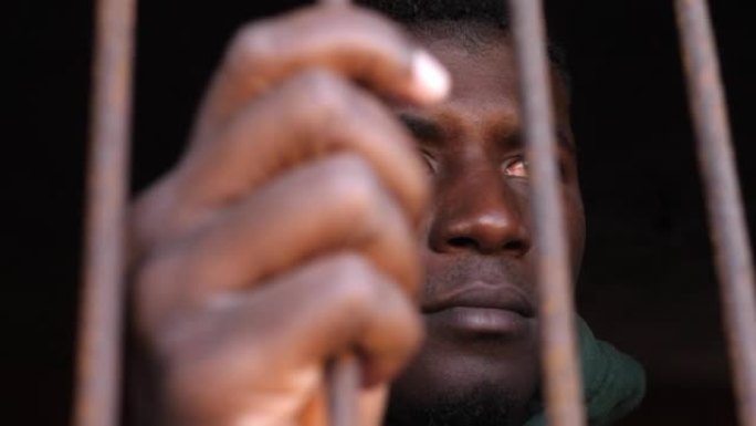 近距离的非洲青年男子在监狱里盯着摄像机。非法移民,人权