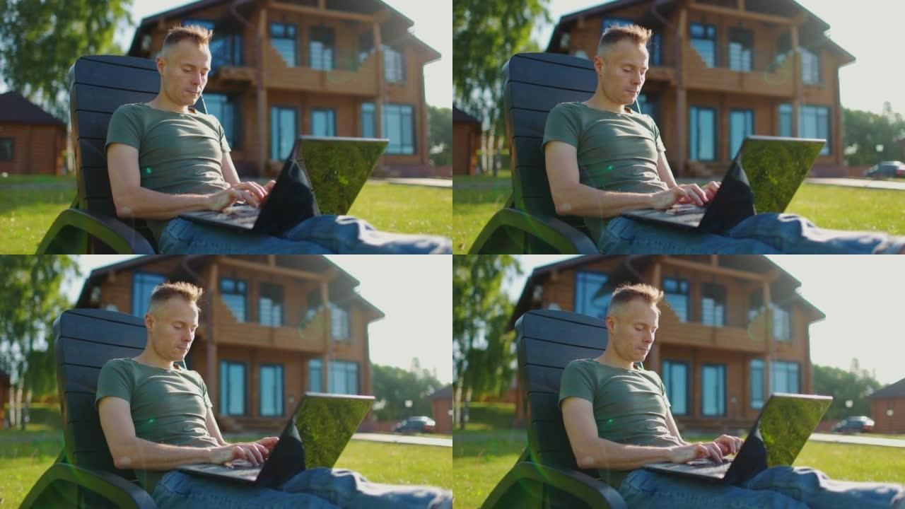 专注的年轻人在乡间别墅院子里的笔记本电脑上工作。在键盘上打字的人。慢动作