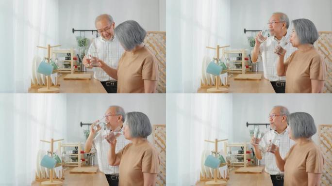 亚洲老年夫妇在家里的厨房里喝一杯水。有吸引力的成熟老年妇女和男子醒来后，在杯子里拿着干净的天然矿物质