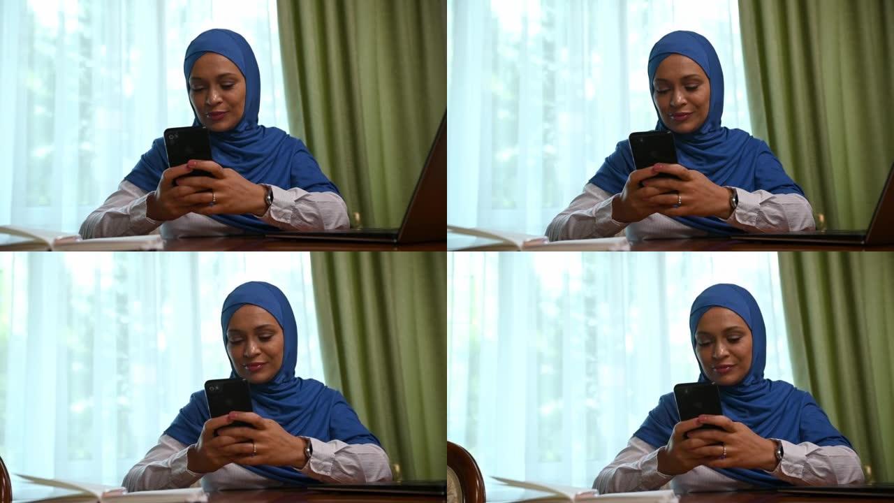 戴头巾的迷人阿拉伯穆斯林妇女，使用手机，滚动新闻提要，浏览网站，检查内容