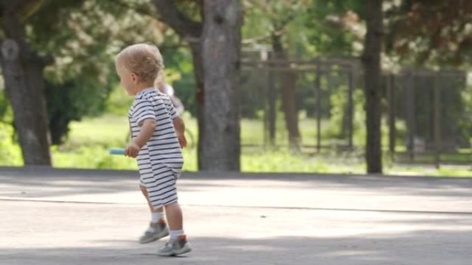 母亲和小孩在夏季公园的沥青上画画很有趣，在阳光明媚的日子里，蹒跚学步的男孩在小径上玩彩色人行道上画粉