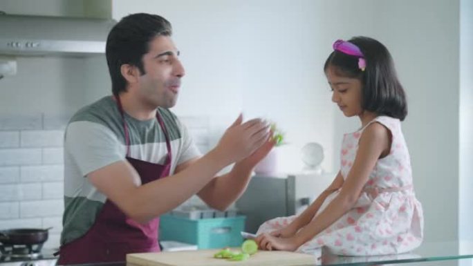 年轻快乐的印度父亲在厨房与女儿互动并准备饭菜