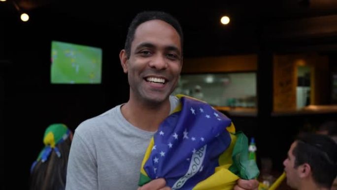 快乐的足球迷在肩膀上举着巴西国旗时对着镜头微笑
