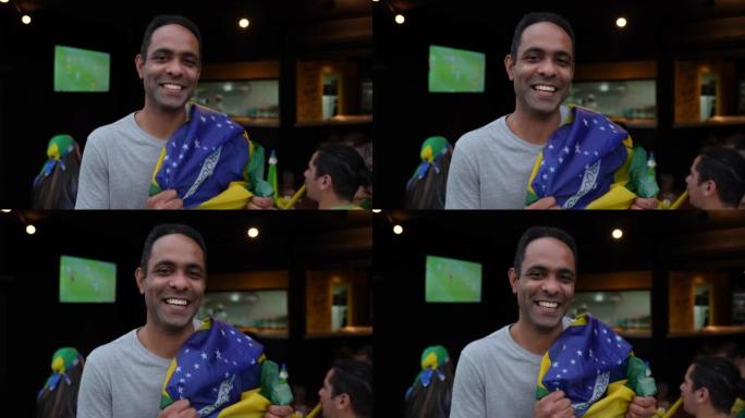 快乐的足球迷在肩膀上举着巴西国旗时对着镜头微笑