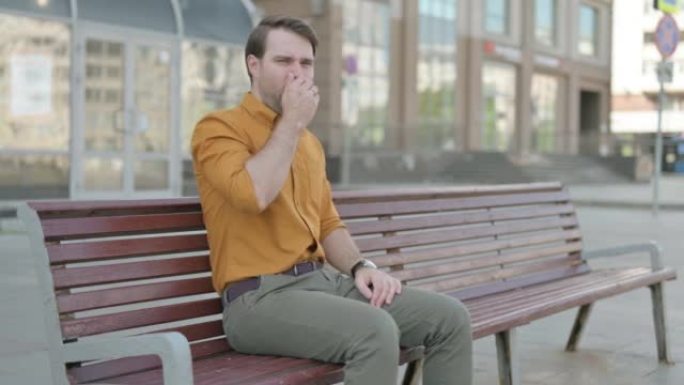 年轻人坐在户外长凳上咳嗽
