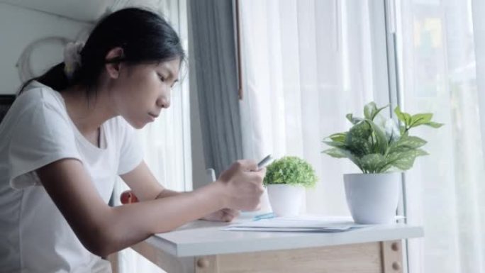 亚洲少女在家通过窗户附近的智能手机观看病毒视频或电影，生活方式概念。