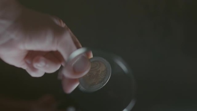 男人拿着放大镜，透过放大镜看一枚欧元硬币，选择性聚焦，近景，深色背景