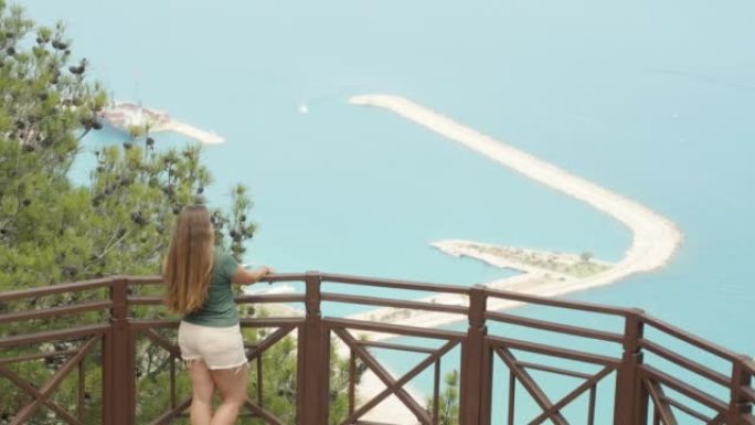 一个女孩站在山顶的栏杆上。她把手指在海里的某个地方。夏季散步。