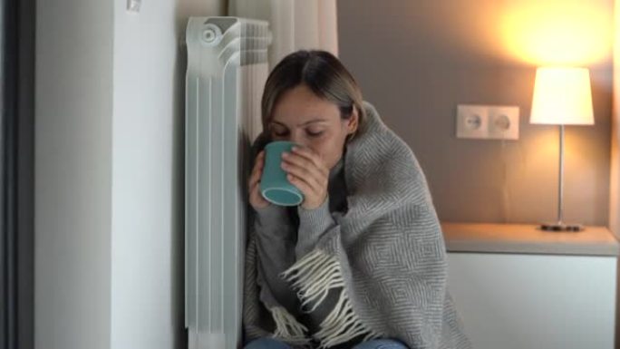 女人依sn在电池上试图热身，并用毯子握住一杯热饮料。
