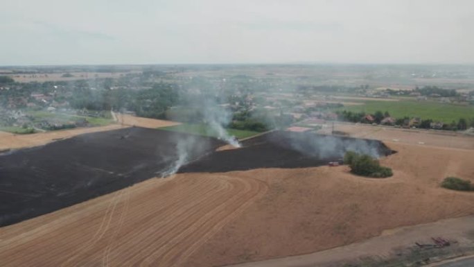 一场庄稼着火后几乎熄灭了。直升机的鸟瞰图。摄像机移开了。棕灰色的烟雾和红色的小火焰。消防员的团队合作