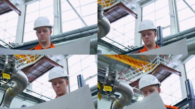 一位戴着白色头盔和工作服的年轻工程师在车间的工作场所检查了技术方案。在工厂为年轻的专业人士工作。工业