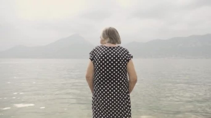 老年妇女在阴霾中看着加尔达湖，抵御山脉