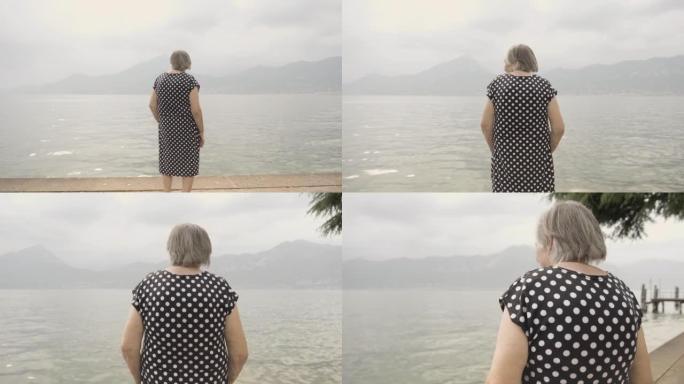 老年妇女在阴霾中看着加尔达湖，抵御山脉