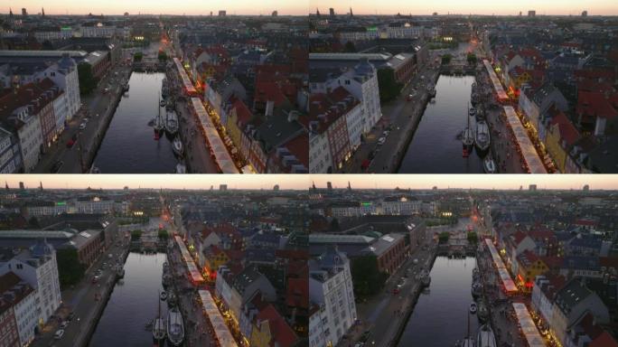前锋在晚上Nyhavn上空飞行。明亮的彩色联排别墅，酒吧和餐馆在城市的水渠旁。丹麦哥本哈根