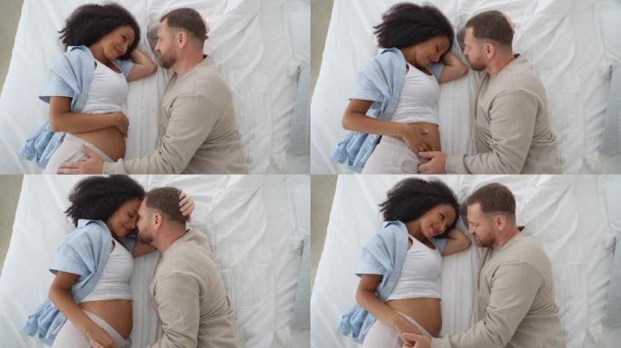 顶视图怀孕的多种族夫妇躺在床上，一起等待分娩。丈夫对女友的温柔照顾。健康怀孕概念