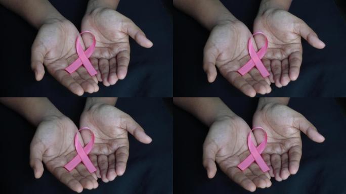 黑色背景手掌上的粉红丝带乳腺癌意识图标徽章。世界癌症日，10月粉红日，全国癌症幸存者日概念。