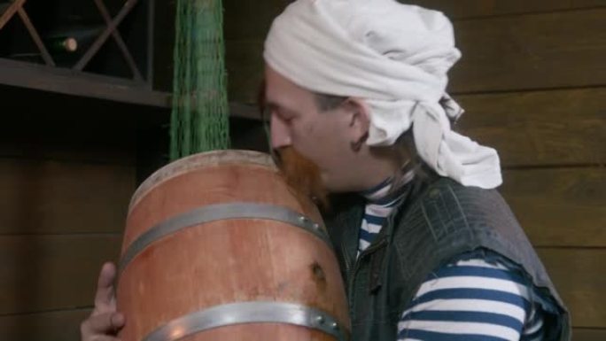 开朗的海盗，头上留着红色的长胡子和头巾，从地窖里拿出一桶朗姆酒，高兴地亲吻了它，期待着一杯好酒和有趣