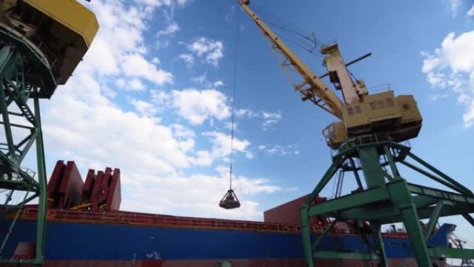 在海港的起重机上，用双绳双勺翻盖式抓斗从集装箱到货舱的谷物转运。小麦装运与水运。农产品运输。