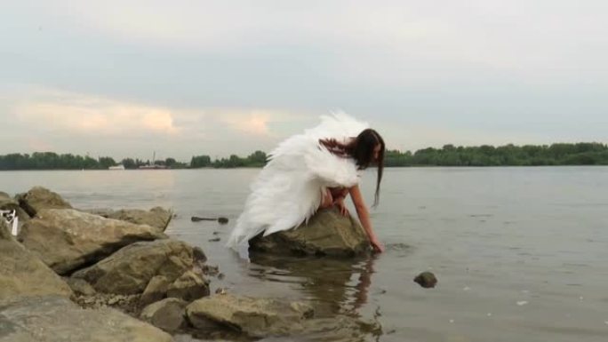 一个年轻的美丽的女人，在河上的一块巨石上有一个白色的翅膀的天使的形象