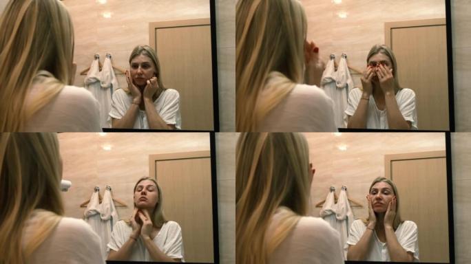 衰老。皮肤松弛。一名年轻女子通过照镜子做整容运动。面部建筑。现代护理，放松面部肌肉。整容，整形手术