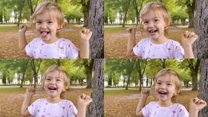 夏天站在公园里看着相机的小女孩。小女孩一边看着镜头一边笑。脸和眼睛有趣的孩子。