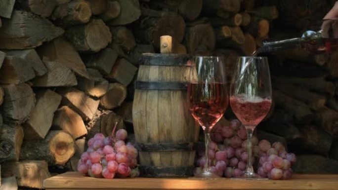 将玫瑰酒倒入装有粉红色葡萄的木制桌子上的葡萄园的玻璃杯中。侍酒师将甜点酒倒入玻璃杯中。酒厂。品酒。填