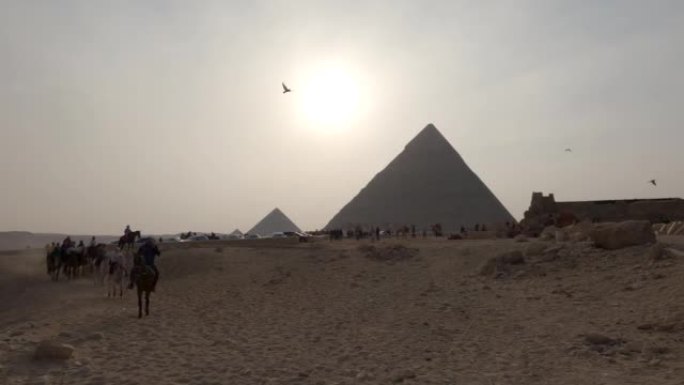 日落时雾霾笼罩的吉萨金字塔建筑群的神秘景色。骑马的游客。