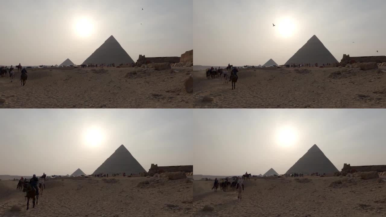 日落时雾霾笼罩的吉萨金字塔建筑群的神秘景色。骑马的游客。
