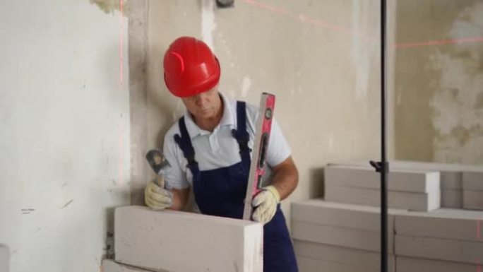 瓦工使用橡胶槌锤敲击和调平混凝土砌块墙。承包商使用精确的气泡和激光水平仪进行砖砌。工人在新公寓房地产