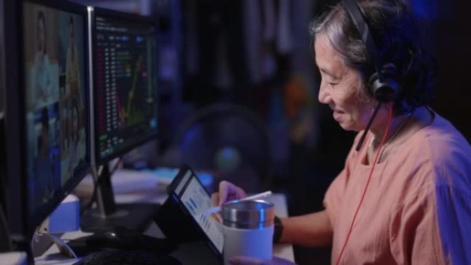 退休亚洲高级女性戴耳机晚上坐在电脑前学习加密股票市场交流在线导师培训课程在家通过视频电话会议